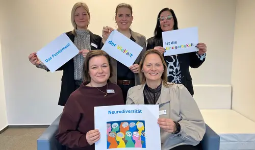 Fünf Menschen halten verschiedene Schilder zu Themen des Fachdienstes Neurodiversität in die Höhe