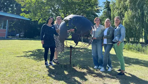 Fünf Frauen stehen um eine Skulptur auf dem Gelände des BBW, die wie eine Weltkugel geformt ist